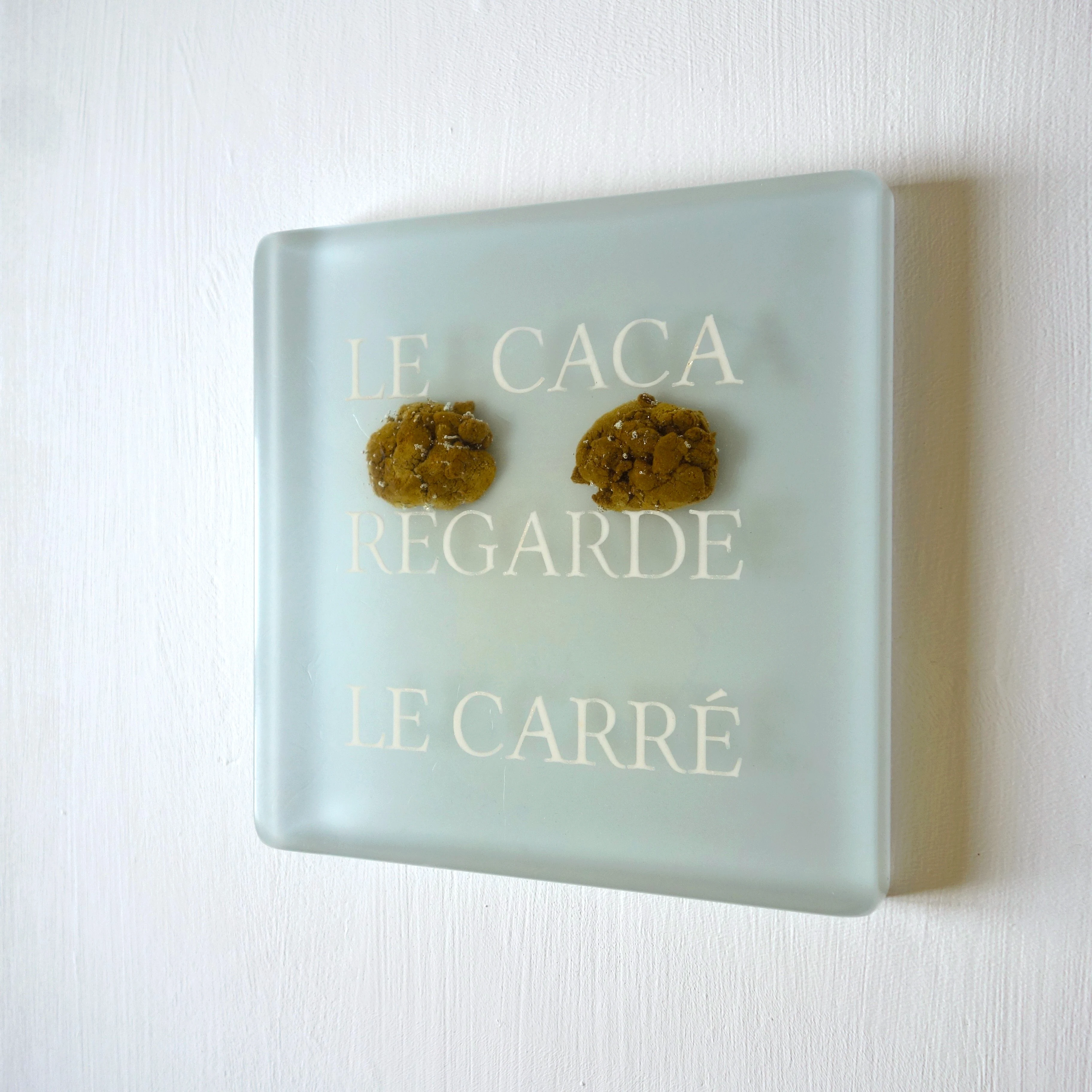 Un tableau carré en verre peint en rouge rosé sur l'envers. La peinture est grattée pour écrire : . Vue de face.