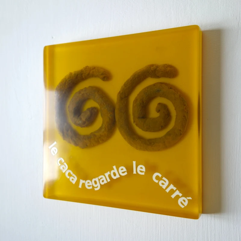 Un tableau carré en verre peint en blanc sur l'envers. La peinture est grattée pour écrire : . Vue de face