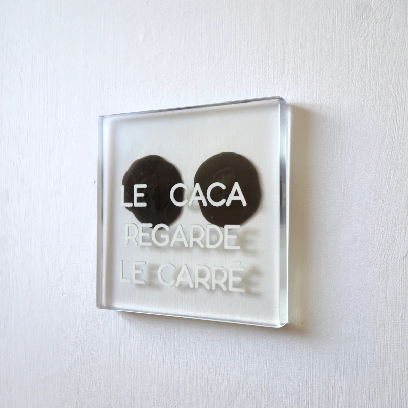 Un tableau carré en verre peint en blanc sur l'envers. La peinture est grattée pour écrire : . Vue de face