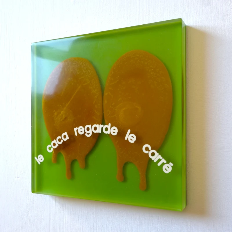 Un tableau carré en verre peint en rouge rosé sur l'envers. La peinture est grattée pour écrire : . Vue de face.