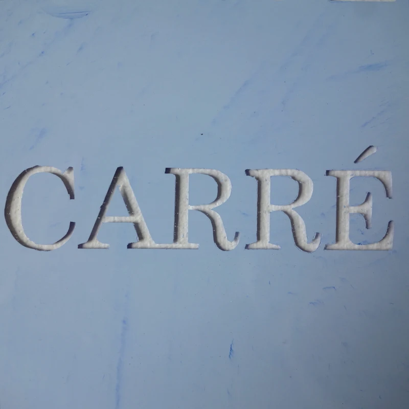 Un tableau carré en verre peint en bleu sur l'envers. La peinture est grattée pour écrire : le caca regarde le carré. Vue de détail.